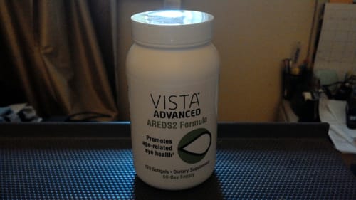 Reviewer's white bottle of VISTA Advanced AREDS2 Formula supplement on a desk.