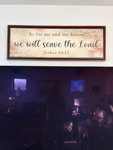 Customer's We Will Serve The Lord sign mounted on a white wall above their large television.