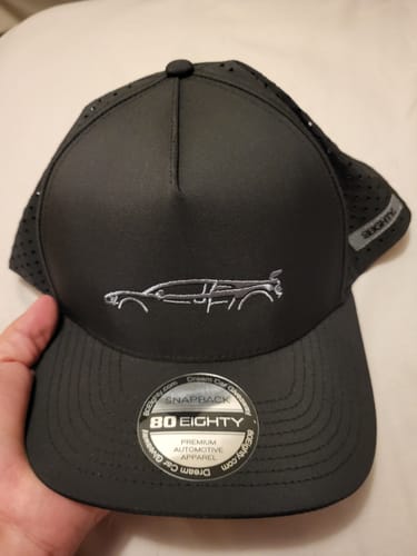 Customer holding the black 80Eighty® Limited Edition DCG89 Hat, showing the embroidered car logo and perforated side panels.