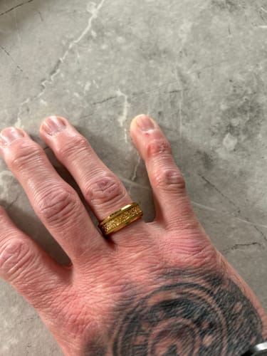 A reviewer's tattooed hand wearing the gold Aureum ring with a textured foil inlay on a marble surface.