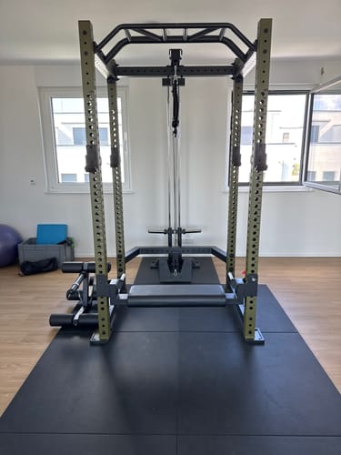 Rezensent zeigt das R8 BlackHawk Power Rack in Militärgrün, fertig aufgebaut in einem Heimstudio.