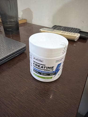 Customer's white tub of Wellcore Creatine Monohydrate sitting on a dark wooden desk.