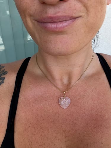 A reviewer wearing a heart-shaped crystal necklace with a gold chain, worn high on the chest.