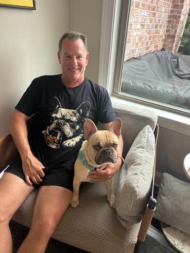 A customer wearing the Whiskey Frenchie Grunge T-Shirt sits in a chair with a French bulldog.