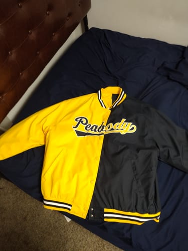 Reviewer's custom split-color varsity jacket in black and gold, with 'Peabody' stitched across the chest, laid out on a bed.