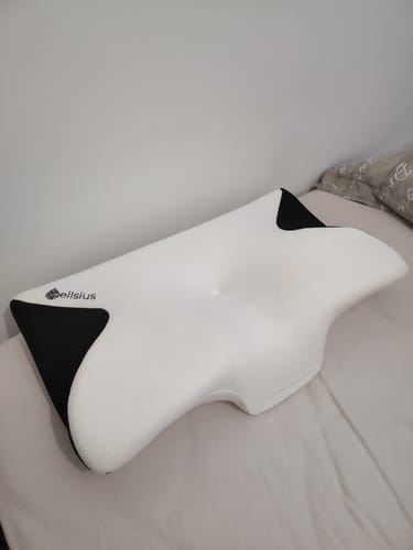 Photo d'un client de l'oreiller Papillon Cervical Cellsius, de couleur blanche et noire, posé sur un lit.