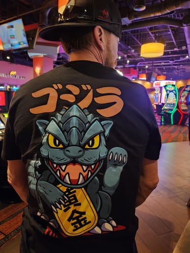 Reviewer showing the back of the black LUCKY ZILLA TEE with its large graphic of a Godzilla-style lucky cat.