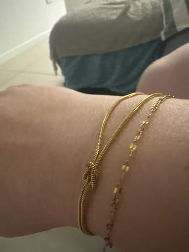 Close-up of a reviewer's wrist wearing a gold knot bracelet stacked with a chain bracelet.