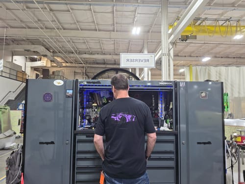 Reviewer from behind wearing the black 80Eighty® DCG89 Shirt with a purple car graphic in a workshop.