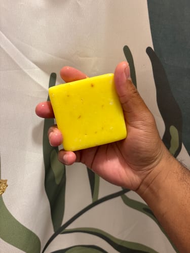 Reviewer holding the square yellow Iron Paradise Bar Soap in their hand.