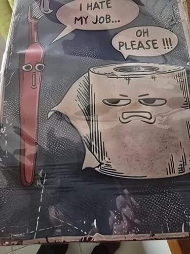 Reviewer shows the 'I Hate My Job Oh Please' funny wall art, which arrived bent and damaged inside its plastic packaging.
