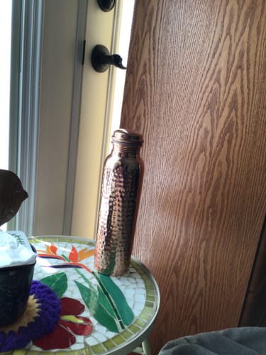 Customer's hand-hammered copper water bottle sitting on a decorative mosaic table.