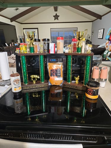 Customer's collection of BBQ products and two large competition trophies displayed on a kitchen stovetop.