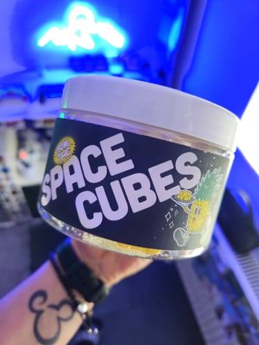 Kunde hält die Dose der THC Space Cubes in der Hand vor einem unscharfen, blauen Hintergrund.
