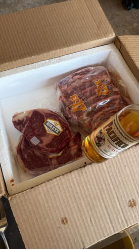 Cliente mostrando su Kit Carne Asada en la caja con los cortes de carne empacados al vacío.