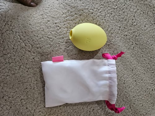 Reviewer's yellow Lem Clitoral Massager displayed with its white storage pouch.
