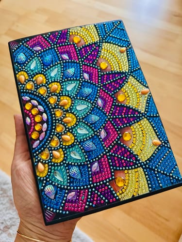 Rezensent zeigt das fertiggestellte, bunte Notizbuch Mandala aus Blumen in der Hand.