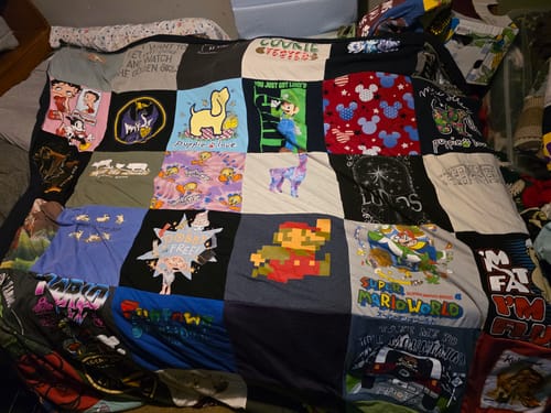 Customer's colorful Project Repat T-Shirt Quilt with various character shirts, including Mario and Betty Boop, laid out on a bed.