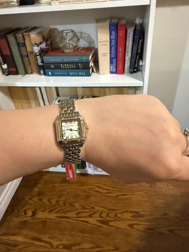 Reviewer showing the two-toned Grealy De Mains watch on their wrist in front of a white bookshelf.
