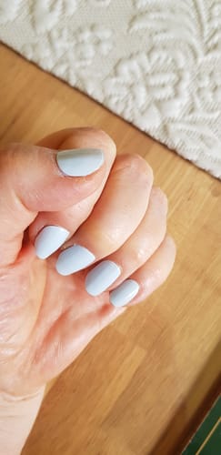 Hand einer Kundin, die die hellblauen „Sea Foam Blue“ UV-Gel-Nagelfolien auf kurzen, runden Nägeln trägt.