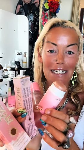 Reviewer smiling while holding up the pink products and boxes from the Instant Glow Kit.