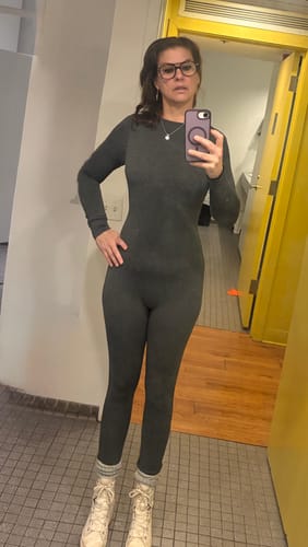 Reviewer taking a mirror selfie in the dark gray NW Sculpt Jumpsuit, styled with light-colored boots.