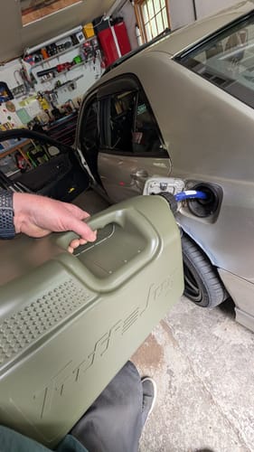 Customer pouring from the green 5 Gallon Jug into a car's fuel tank in a garage.