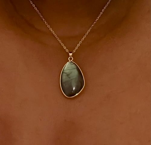 Gros plan du collier en Labradorite avec un pendentif en pierre sombre, porté par une cliente.