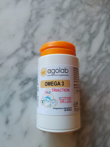 Il cliente mostra un flacone bianco di Omega 3 Tri-Action con tappo arancione, su una superficie di marmo.