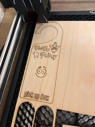 Customer's laser cutter engraving a wooden 'Tooth Fairy' door hanger on a honeycomb bed.
