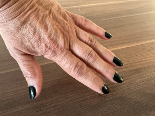 Hand einer Kundin mit aufgetragenen, glänzend schwarzen Midnight Waltz UV-Gel-Nagelfolien.