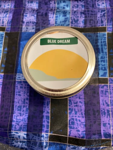 Customer's round, sealed tin of Blue Dream on a blue and purple plaid fabric.