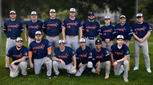 A customer's baseball team posing together in their custom navy blue and orange authentic baseball jerseys on a field.