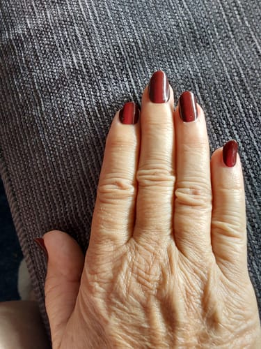 Nahaufnahme der Hand einer Kundin mit glänzender, rubinroter Ruby CatEye UV-Gel-Maniküre.