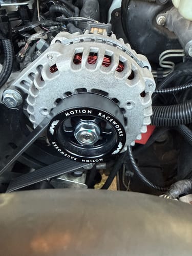 Customer's black LS Billet Overdrive Alternator Pulley installed on the front of a silver alternator in an engine bay.