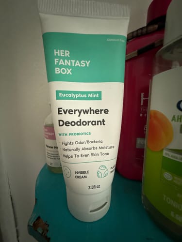 Customer's tube of Everywhere Deodorant standing on a teal surface among other personal care products.