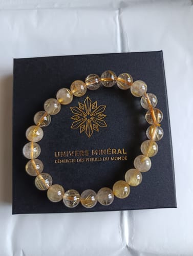 Le Bracelet en Quartz Rutile d'un client est posé sur sa boîte noire, montrant ses perles claires à inclusions dorées.
