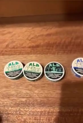 Partial view of Customer's tins of Chilled Mint Nicotine Pouches on a wooden surface.
