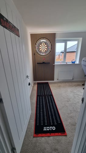 Customer's acoustic slatted wall panel used as a stylish backdrop for a dartboard setup in a room.