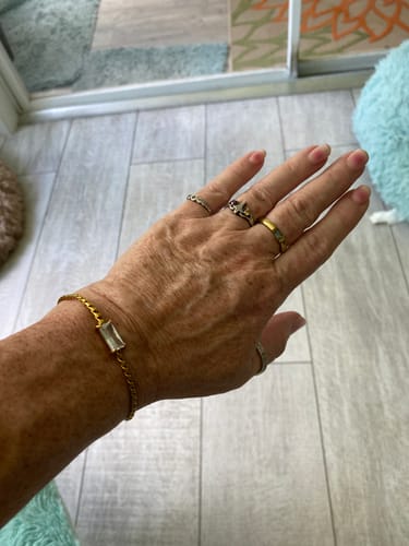 A reviewer's hand showing the delicate gold Castellanos Bracelet with a rectangular gem on their wrist.