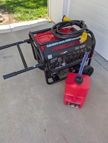 Customer's red 5 Gallon Jug with its spout, sitting next to a large generator on a concrete surface.
