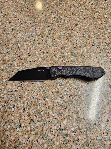 Customer's Kizer Wharning Folding Knife with a black blade and patterned handle with a purple accent on a counter.