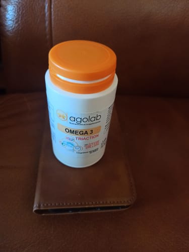 Il flacone di Omega 3 del cliente, bianco con tappo arancione, su una superficie in pelle marrone.