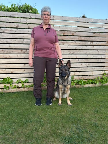 Anmelder iført brune 2-in-1 Zip-Off Skalbukser, som viser pasformen i fuld figur udendørs ved siden af en hund.