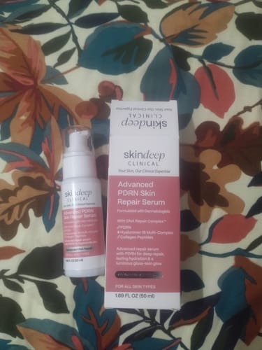 Reviewer's bottle of Advanced PDRN Skin Repair Serum placed next to its packaging on a floral surface.