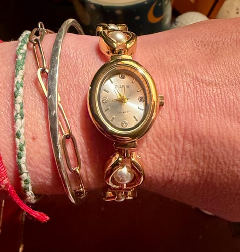 Reviewer wearing the gold PERLE DE MAINS watch on a wrist stacked with several other bracelets.