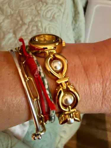 A customer's wrist showing the PERLE DE MAINS watch band, highlighting the gold links with inset pearls.
