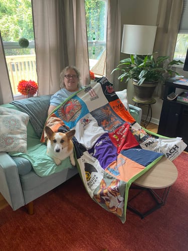 Customer and their dog on a couch, covered by a colorful Project Repat T-Shirt Quilt.