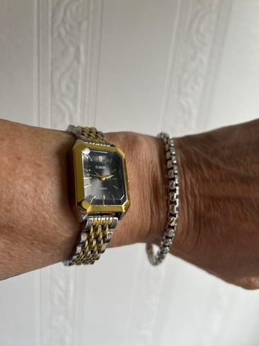 Customer wearing the CLAIRE DE MAINS watch with a black face and a two-tone gold and silver strap.