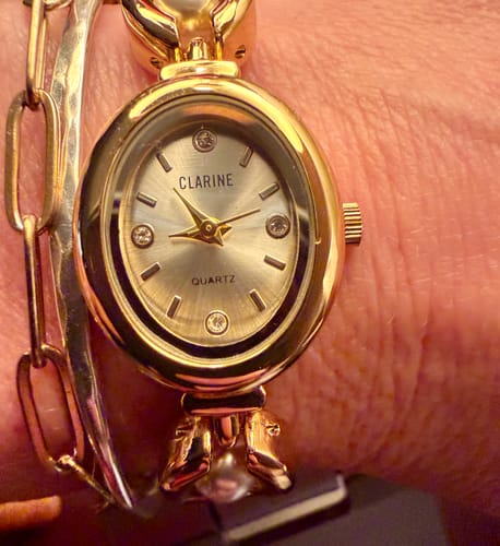 Close-up of a reviewer's PERLE DE MAINS watch, showing the oval face and gold band on their wrist.